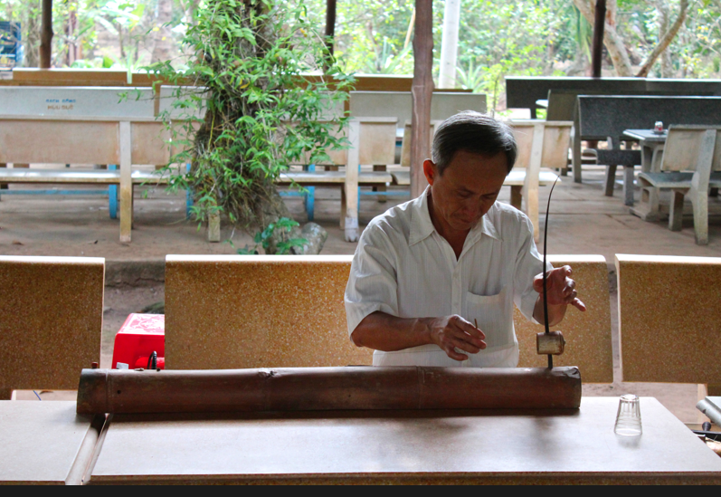 A local Vietnamese man plays the đàn bầu, a Vietnamese monochord, or one-string guitar creating oriental, violin-like sound.