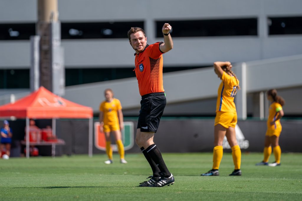 A referee points at and dances with Sebastian the Ibis to the pre-game music before the start of Miami’s match versus Pittsburgh at Cobb Stadium on Sept. 26, 2021.