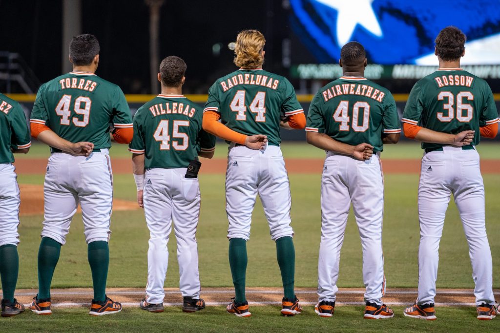 Canes baseball players stand for the playing of the national anthem before the start of their game versus Towson at Mark Light Field on Feb. 18, 2022.