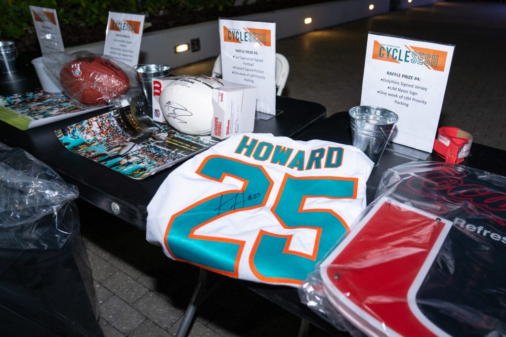 Raffle prizes, including signed Dolphins memorabilia, Adidas gear and one week of priority parking on campus sit on a display table during the Team Hurricanes Dolphins Challenge Cancer Cycle Sesh at the Lakeside Patio on Feb. 24, 2022.