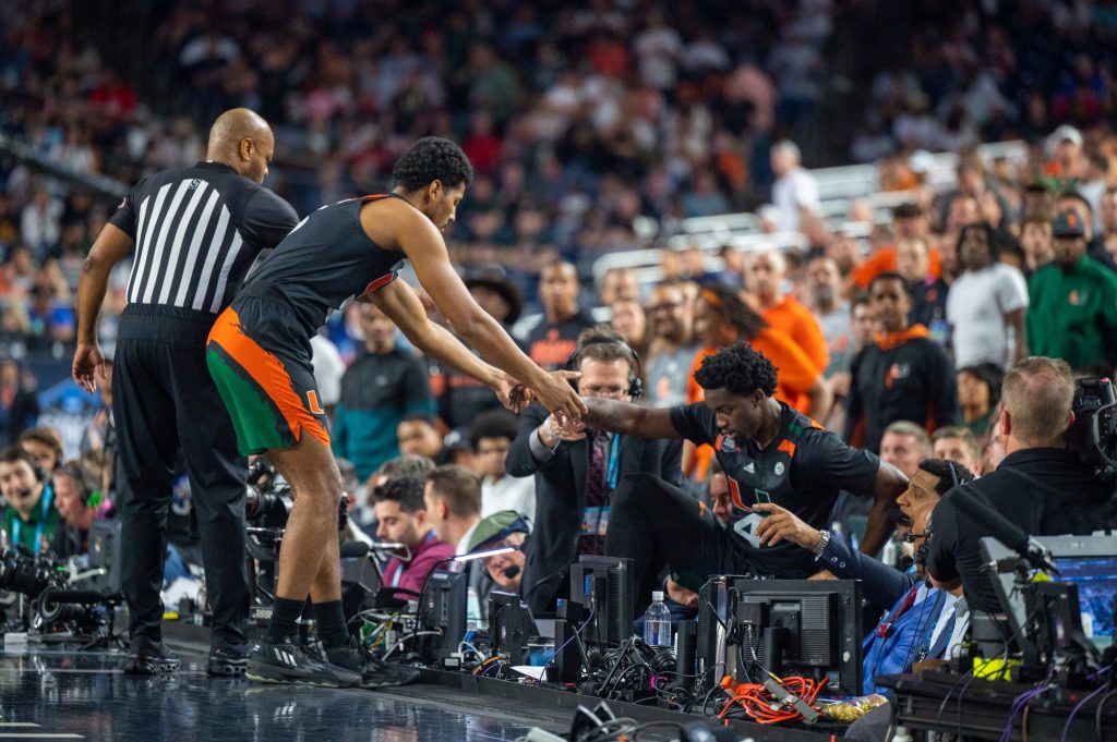 Sophomore guard Bensley Joseph is helped up by teammate Harlond Beverly after falling off the court during the first half of Miami's Final Four loss to the University of Connecticut on Saturday, April 1 at the NRG Stadium.